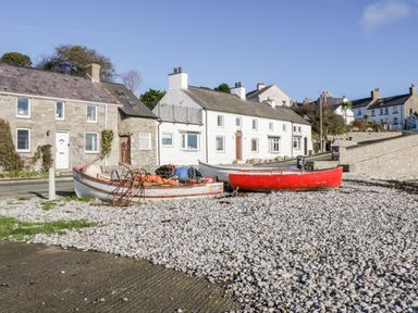 Three small boats on a pebble beach near stone and white houses at Halcyon in Moelfre near Benllech