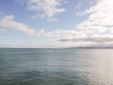 An expansive view of a sea under a partly cloudy sky with distant land visible at Halcyon Moelfre near Benllech