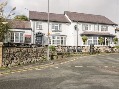 An exterior view of a two-story white building with wooden picnic tables outside and a stone retaining wall Kinmel Arms Moelfre near Benllech