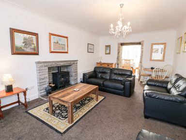 A living room with black leather sofas a wooden coffee table a stone fireplace and a dining area at Halcyon Moelfre near Benllech