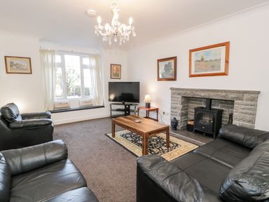 A living room with black leather sofas a wooden coffee table a stone fireplace and a television at Halcyon in Moelfre near Benllech