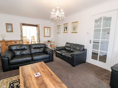 A living room with two black leather sofas a wooden coffee table and a dining area at Halcyon in Moelfre near Benllech