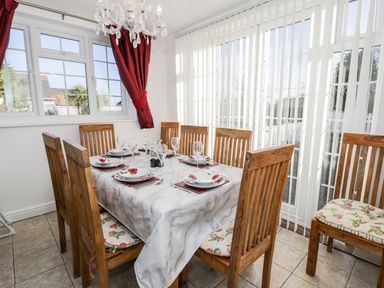 A dining room with a table set for six and wooden chairs with floral seat cushions at Halcyon in Moelfre near Benllech