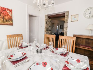 A dining room with a marble table set with plates glasses and wooden chairs at Halcyon in Moelfre near Benllech