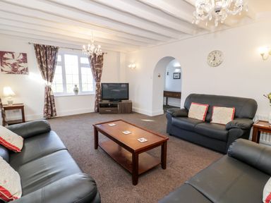 A living room with three leather sofas a wooden coffee table a television and patterned curtains at Halcyon in Moelfre near Benllech