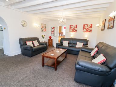 A living room with three black sofas a wooden coffee table and floral wall art at Halcyon Moelfre near Benllech