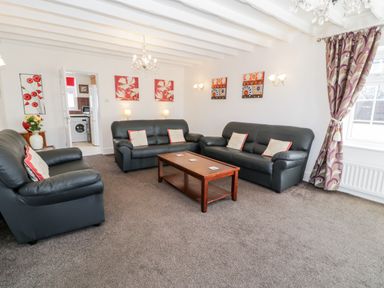A living room with black leather sofas wooden coffee table and patterned curtains at Halcyon Moelfre near Benllech