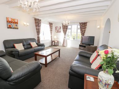 A living room with black leather sofas a coffee table a television and floral curtains at Halcyon Moelfre near Benllech
