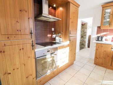 A kitchen with wooden cabinets a stainless steel oven a stovetop and brown tiled backsplash at Halcyon in Moelfre near Benllech