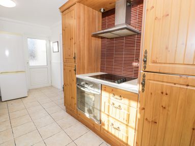 A kitchen with wooden cabinets a built-in oven stovetop range hood tiled floor and a white door at Halcyon Moelfre near Benllech