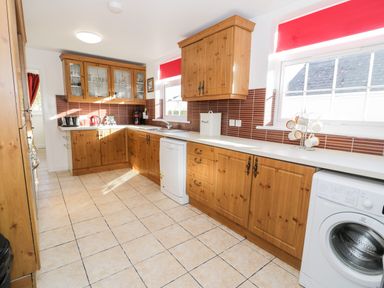 A kitchen with wooden cabinets white countertops tiled floor and appliances at Halcyon Moelfre near Benllech