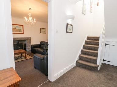 A hallway with carpeted stairs and entrance to a living room with black sofas and a fireplace at Halcyon Moelfre near Benllech