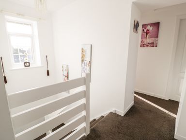 A stairway with white railing and brown carpet with wall art and a window at Halcyon in Moelfre near Benllech