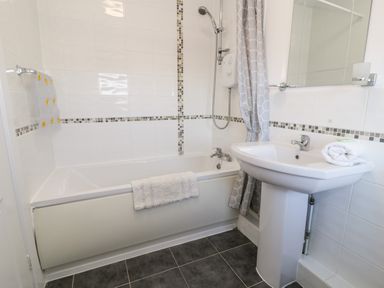 A bathroom with a bathtub a shower a sink with a mirror and towels at Halcyon in Moelfre near Benllech