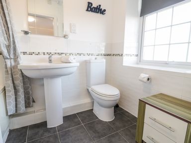 A bathroom with a pedestal sink a toilet a window with blinds a small cabinet and a shower curtain at Halcyon in Moelfre near Benllech