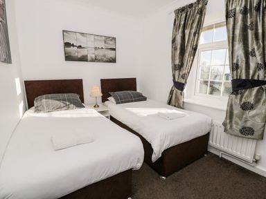 A bedroom with two single beds a window and a nightstand with a lamp at Halcyon in Moelfre near Benllech