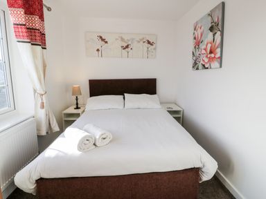 A bedroom with a double bed and two rolled towels with wall art and nightstands at Halcyon Moelfre near Benllech