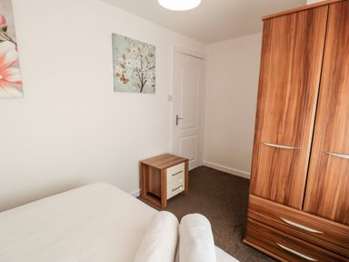 A bedroom with a double bed two rolled towels wooden wardrobe wooden bedside table and wall art at Halcyon in Moelfre near Benllech