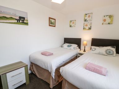 A bedroom with two single beds a nightstand with a lamp and framed pictures on the wall at Halcyon in Moelfre near Benllech