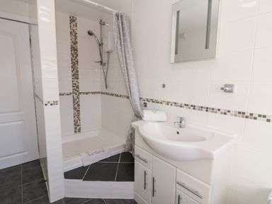 A bathroom with a shower area a sink with storage cabinets and a mirror at Halcyon in Moelfre near Benllech