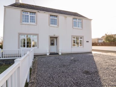The exterior of a two-story house with a gravel driveway and white fence at Halcyon in Moelfre near Benllech