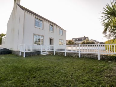 A two-story house with a white exterior and multiple windows a white wooden fence surrounding the front yard with grass and a palm tree Halcyon Moelfre near Benllech