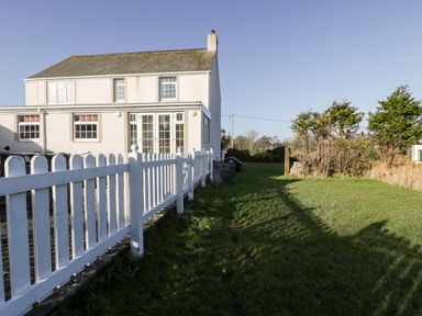 The exterior of a two story house with a white picket fence and a grassy yard at Halcyon Moelfre near Benllech