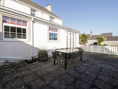 A patio with a black table and six chairs outside a white house with windows and a white picket fence at Halcyon Moelfre near Benllech