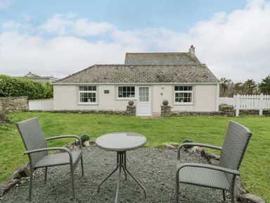 A small outdoor seating area with two chairs and a round table in front of a single-story house at Halcyon Annexe Moelfre near Benllech