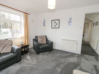 A living room with black leather sofas a side table with lamp and decorative items on a grey carpet at Halcyon Annexe in Moelfre near Benllech