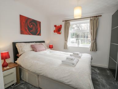 A bedroom with a double bed with pillows and folded towels two bedside tables with red lamps a window with curtains and a wardrobe at Halcyon Annexe in Moelfre near Benllech
