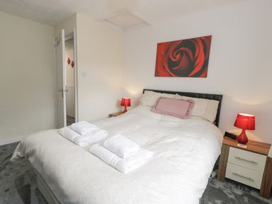 A bedroom with a bed with white bedding bedside tables with red lamps a door and a red rose picture on the wall at Halcyon Annexe in Moelfre near Benllech