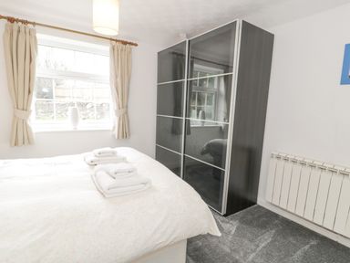 A bedroom with a bed with folded towels on it a window with curtains a black wardrobe and a radiator at Halcyon Annexe in Moelfre near Benllech