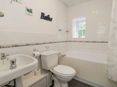 A bathroom with a sink, toilet, bathtub, small window, and wall decoration at Halcyon Annexe Moelfre near Benllech