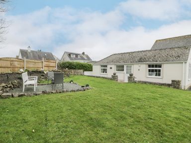 A backyard with a table and chairs on a gravel area and a small cream house at Halcyon Annexe in Moelfre near Benllech