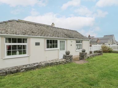 A single story house with three windows a door and a stone fence with grass in front at Halcyon Annexe Moelfre near Benllech