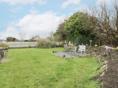 A garden with green grass a white picket fence outdoor seating with two chairs and a bench at Halcyon Annexe Moelfre near Benllech