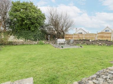 A garden with grass lawn table and chairs near a wooden fence at Halcyon Annexe in Moelfre near Benllech