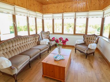 A sitting room with vintage sofas a wooden coffee table a vase with flowers and large windows at Dooneen near Castletownshend County Cork