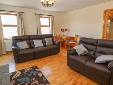 A living room with two brown sofas and cushions a wooden dining table with chairs and vase of flowers at Dooneen near Castletownshend County Cork
