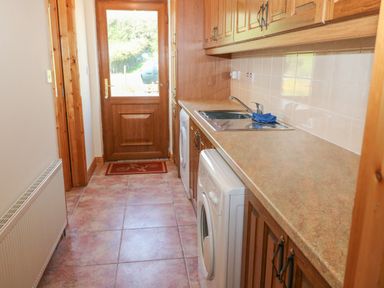 A laundry room with a washing machine sink and cupboards and a door leading outside at Dooneen near Castletownshend County Cork
