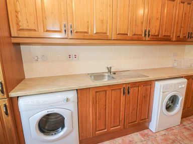 A laundry room with wooden cabinets a sink a washing machine and a dryer at Dooneen near Castletownshend County Cork
