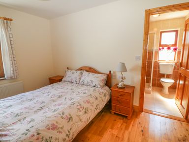 A bedroom with a double bed and floral bedding next to a wooden nightstand with a lamp and an ensuite bathroom at Dooneen near Castletownshend County Cork