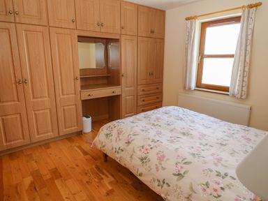 A bedroom with wooden floor built in wooden wardrobes a bed with floral bedding and a window with curtains at Dooneen near Castletownshend County Cork