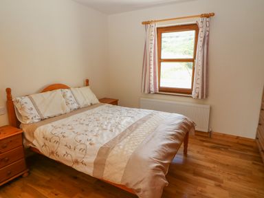 A bedroom with a double bed and wooden bedside tables near a window at Dooneen near Castletownshend County Cork