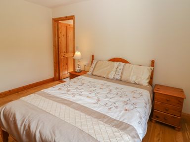 A bedroom with a double bed with a floral bedspread two wooden bedside tables and a wooden door at Dooneen near Castletownshend County Cork