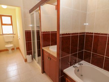 A bathroom with a toilet near a window a shower with glass doors a sink with a wooden cabinet and a bathtub with tiled walls at Dooneen near Castletownshend County Cork