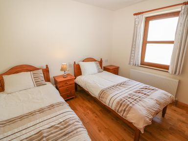 A bedroom with two single beds a lamp on a bedside table and a window with curtains at Dooneen in Dooneen near Castletownshend County Cork