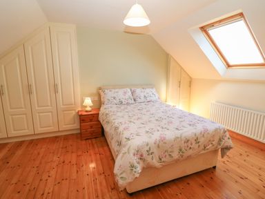 A bedroom with a bed and floral bedding a wooden nightstand with a lamp built in wardrobes and a skylight window at Dooneen near Castletownshend County Cork