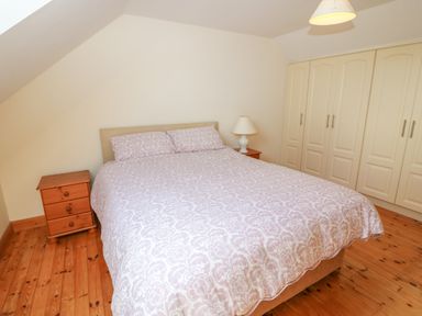 A bedroom with a double bed a bedside table with a lamp a wooden floor and built in wardrobes at Dooneen near Castletownshend County Cork